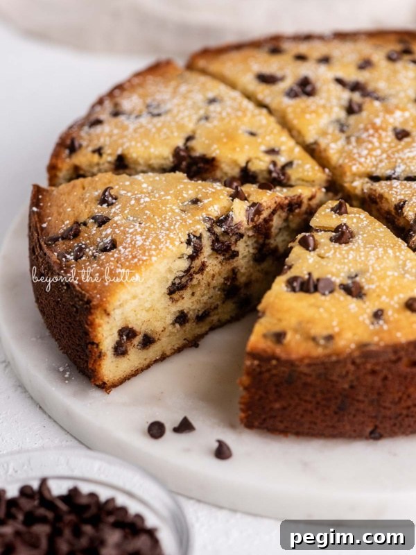 Slices of chocolate chip ricotta cake on a marble cake round with small bowl of mini chocolate chips nearby.