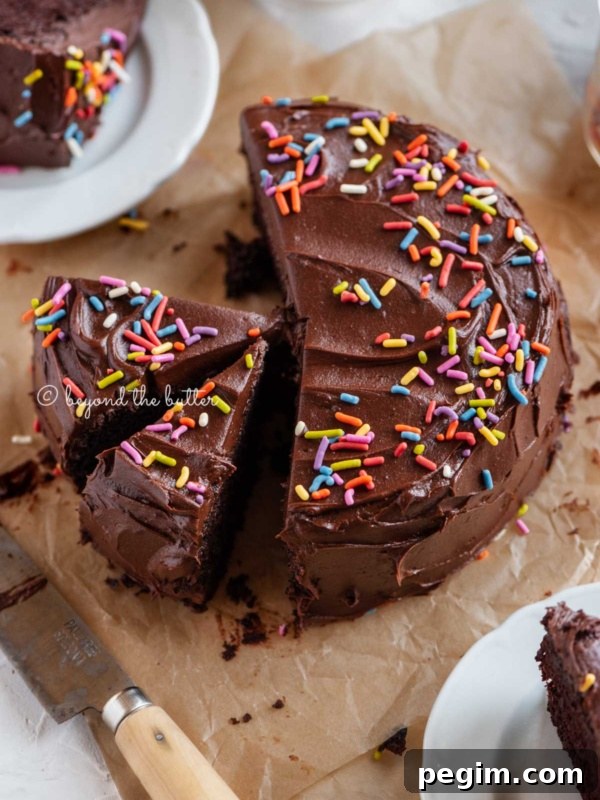 Angled image of sliced single layer chocolate cake on parchment paper with slices of cake on small dessert plates around it and a knife on parchment paper.