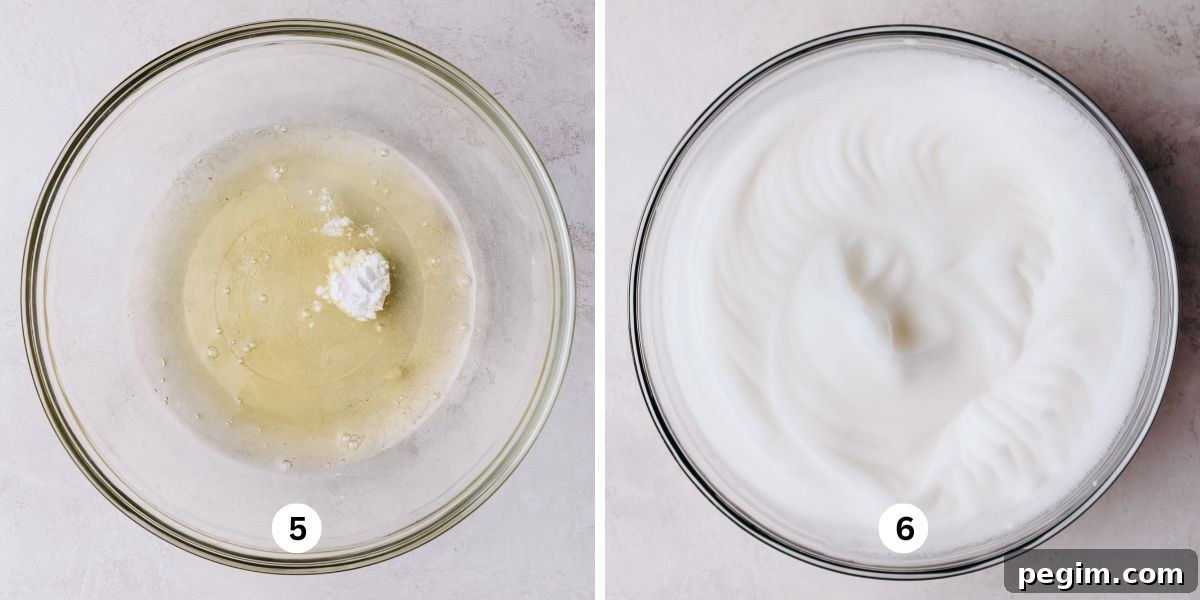 Mixing egg whites and cream of tartar into stiff glossy peaks in a large glass mixing bowl on a white marbled background.