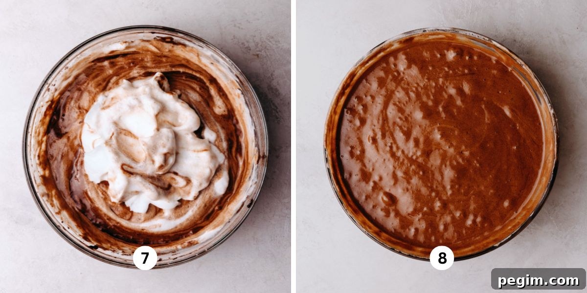 Folding meringue into chocolate chiffon cake batter in a large glass bowl on a white marbled background.