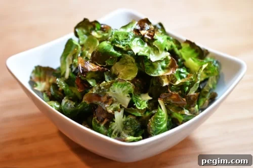 A square bowl is filled with crispy Brussels sprout chips, a paleo and vegan snack