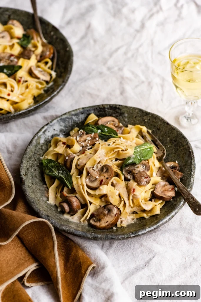 Bowl of pasta mixed with mushrooms and topped with crispy sage leaves with a fork on a linen table.
