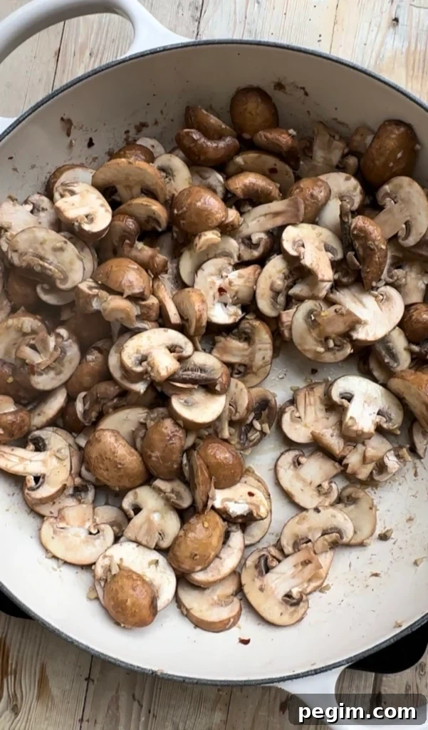 Overhead view of sliced crimini baby bella mushrooms cooking in a large cast iron pan.