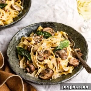 Bowl of pasta mixed with mushrooms and topped with crispy sage leaves with a fork on a linen table.
