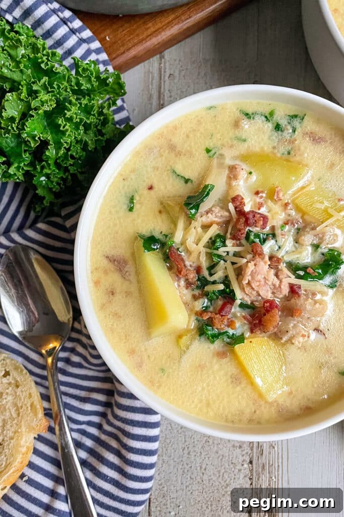 Olive Garden Zuppa Toscana soup in a serving bowl.  Fresh parsley a serving spoon, and slices of bread are placed on the left side of the bowl.