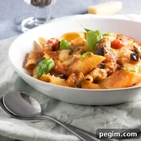 A white bowl of pasta alla norma on a light green tea towel