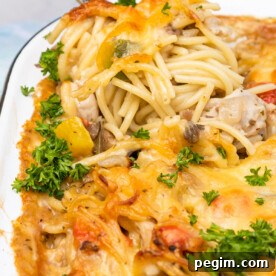 Closeup of a big serving spoon scooping out some cheesy baked chicken spaghetti from a white baking dish