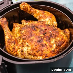 A whole cooked rotisserie style chicken in an air fryer basket