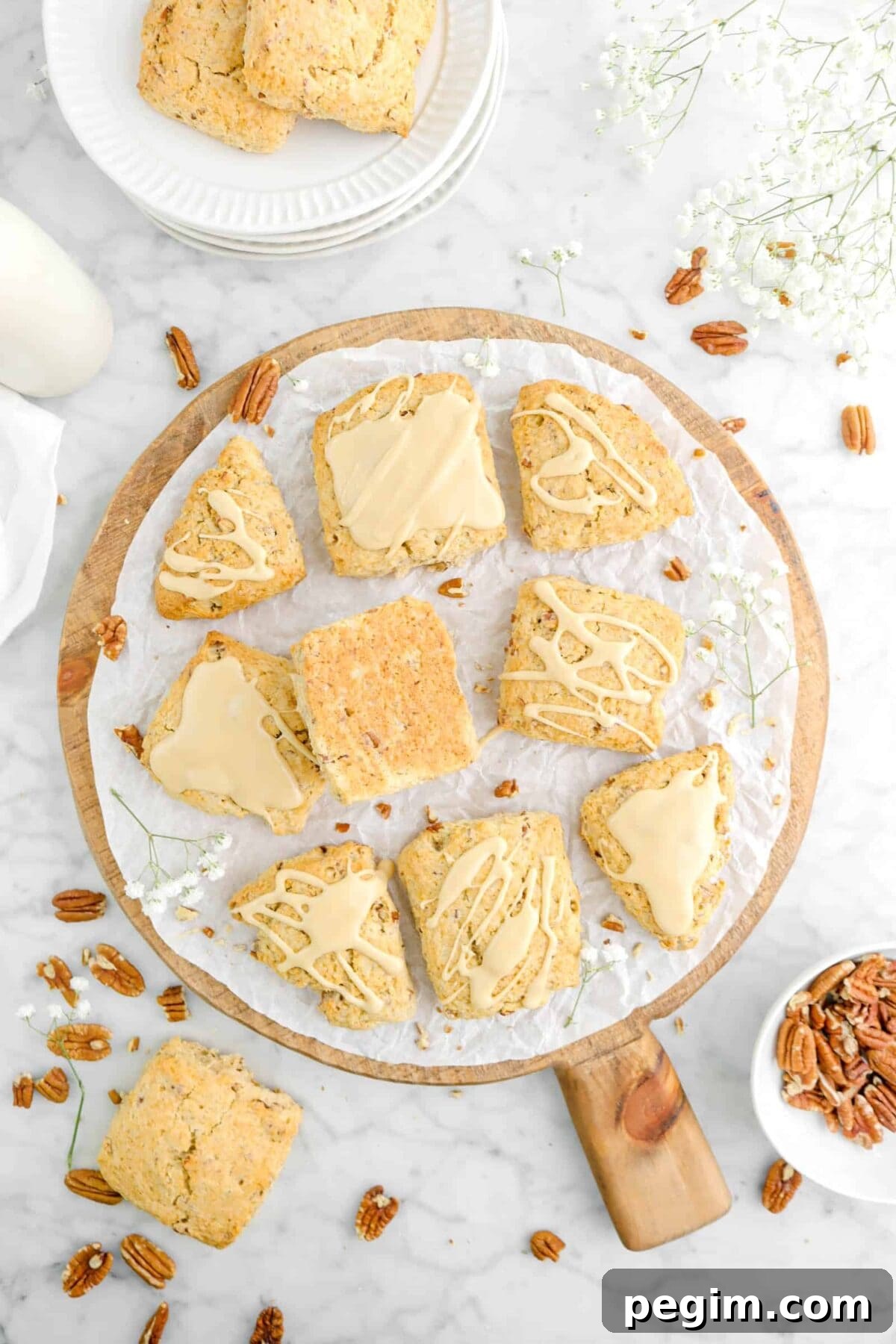 nine glazed maple pecan scones on wood board with flowers, pecans, and more scones around