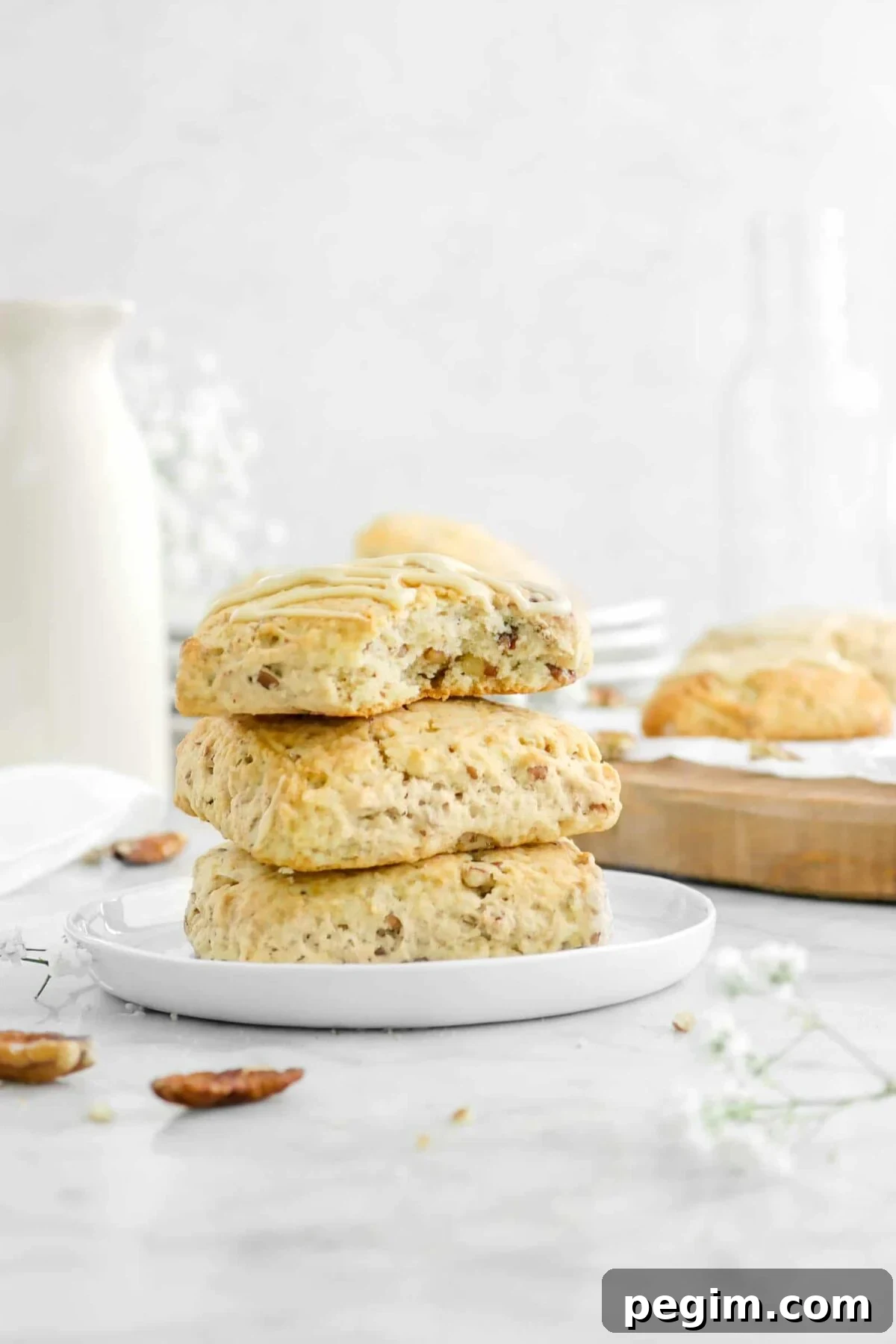 three stacked scones on white plate with a bite missing and flowers around