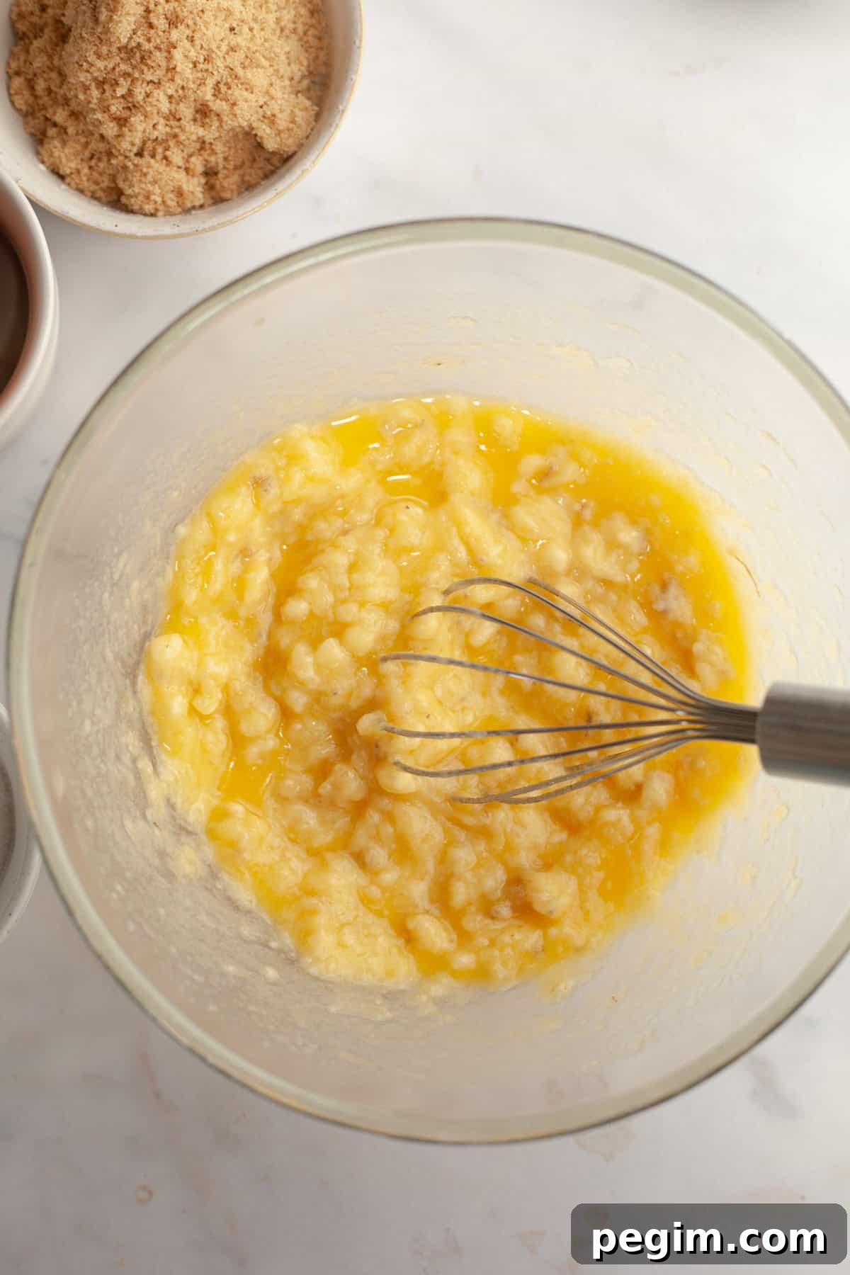 A large glass bowl with butter and mashed banana in it.