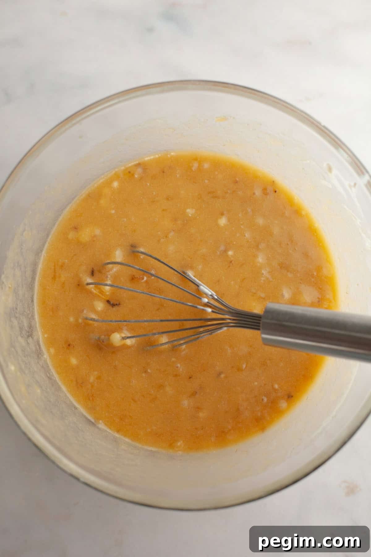 A large glass bowl with a whisk and banana bread batter.
