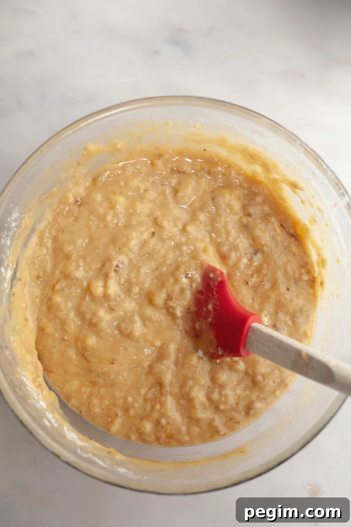 A large glass bowl with a rubber spatula and banana bread batter.