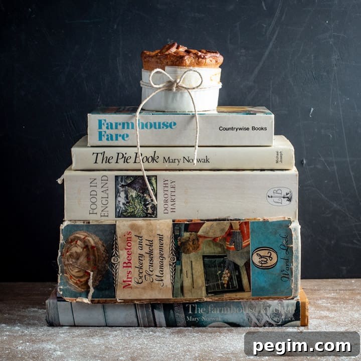 black backdrop with a pile of vintage cookbooks and a single homemade British pork pie balanced on top