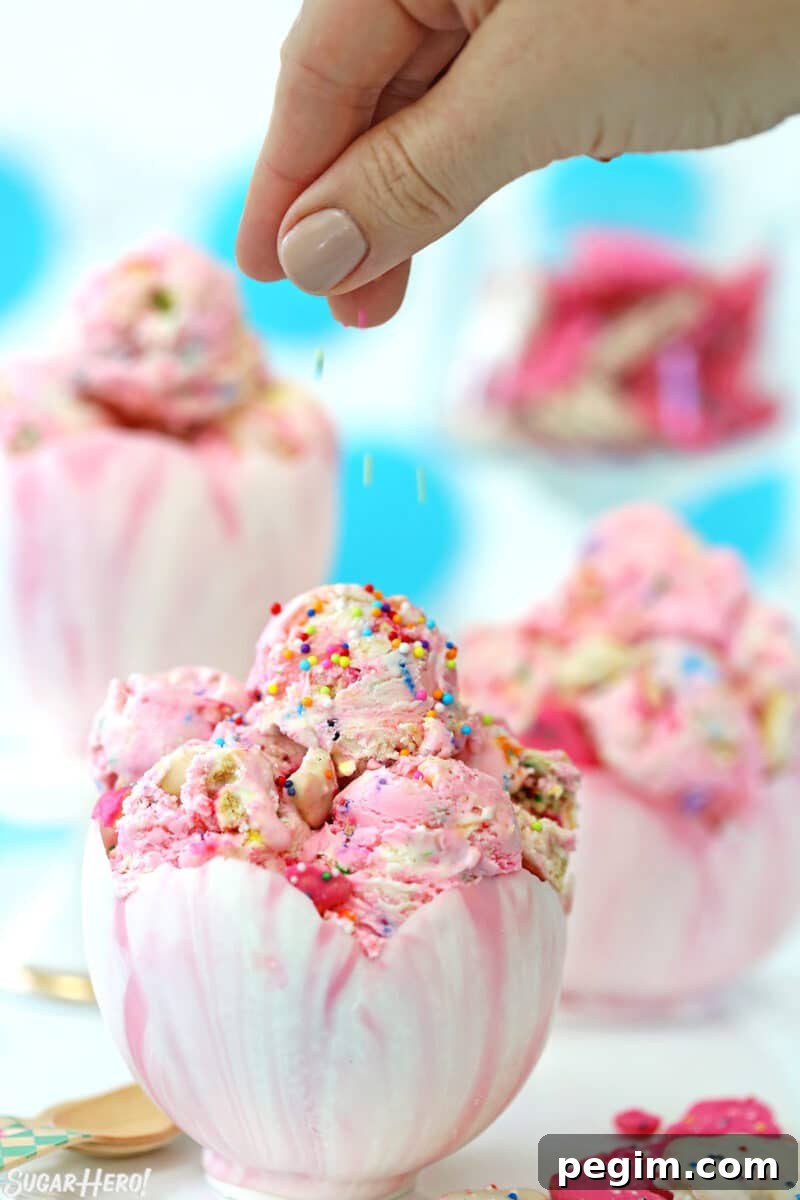 Scoops of Circus Animal No-Churn Ice Cream in a chocolate bowl with a hand sprinkling sprinkles on top.