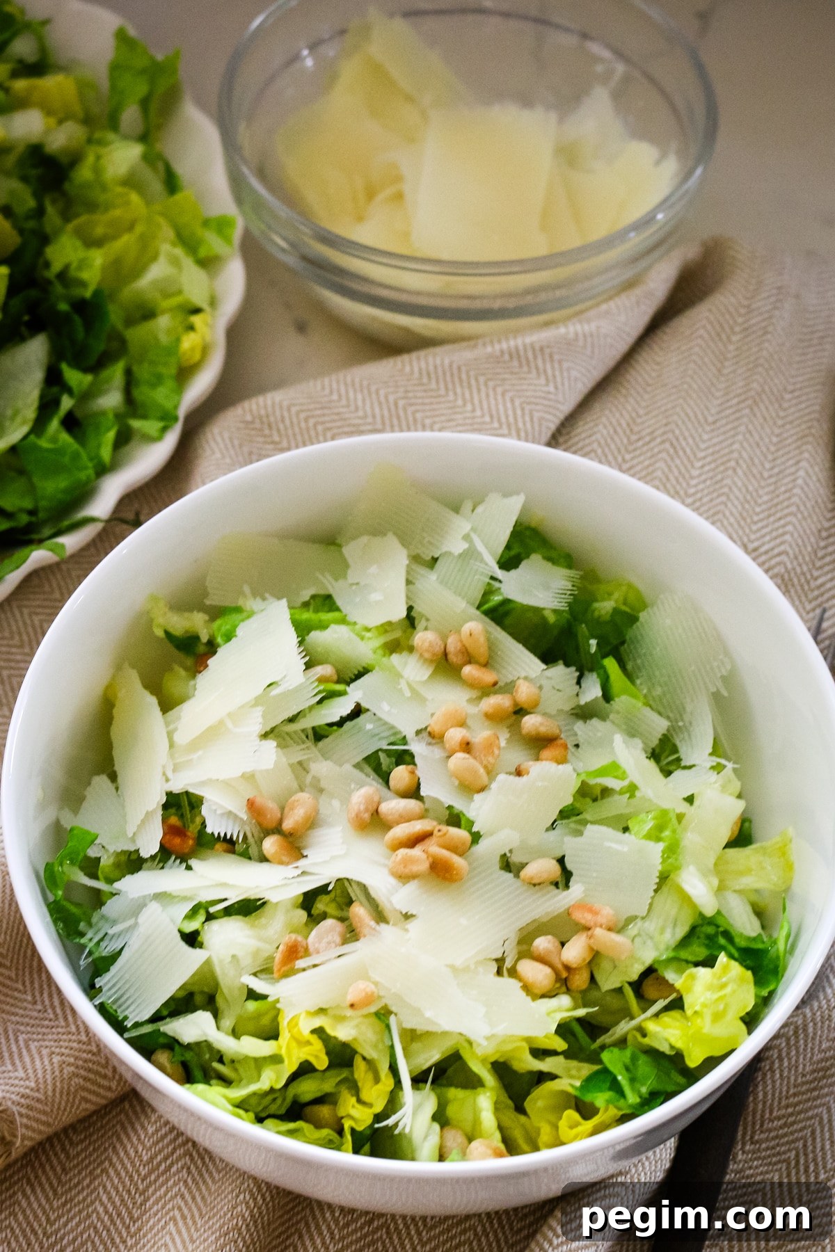 Romaine salad in a white bowl with a fork in it, and a large white plate with romaine salad behind it.