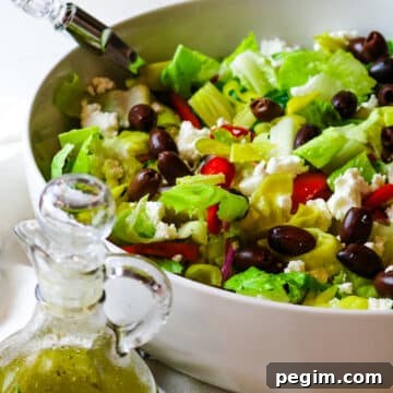 chopped Mediterranean salad in a white bowl with salad dressing on the bottom left corner.