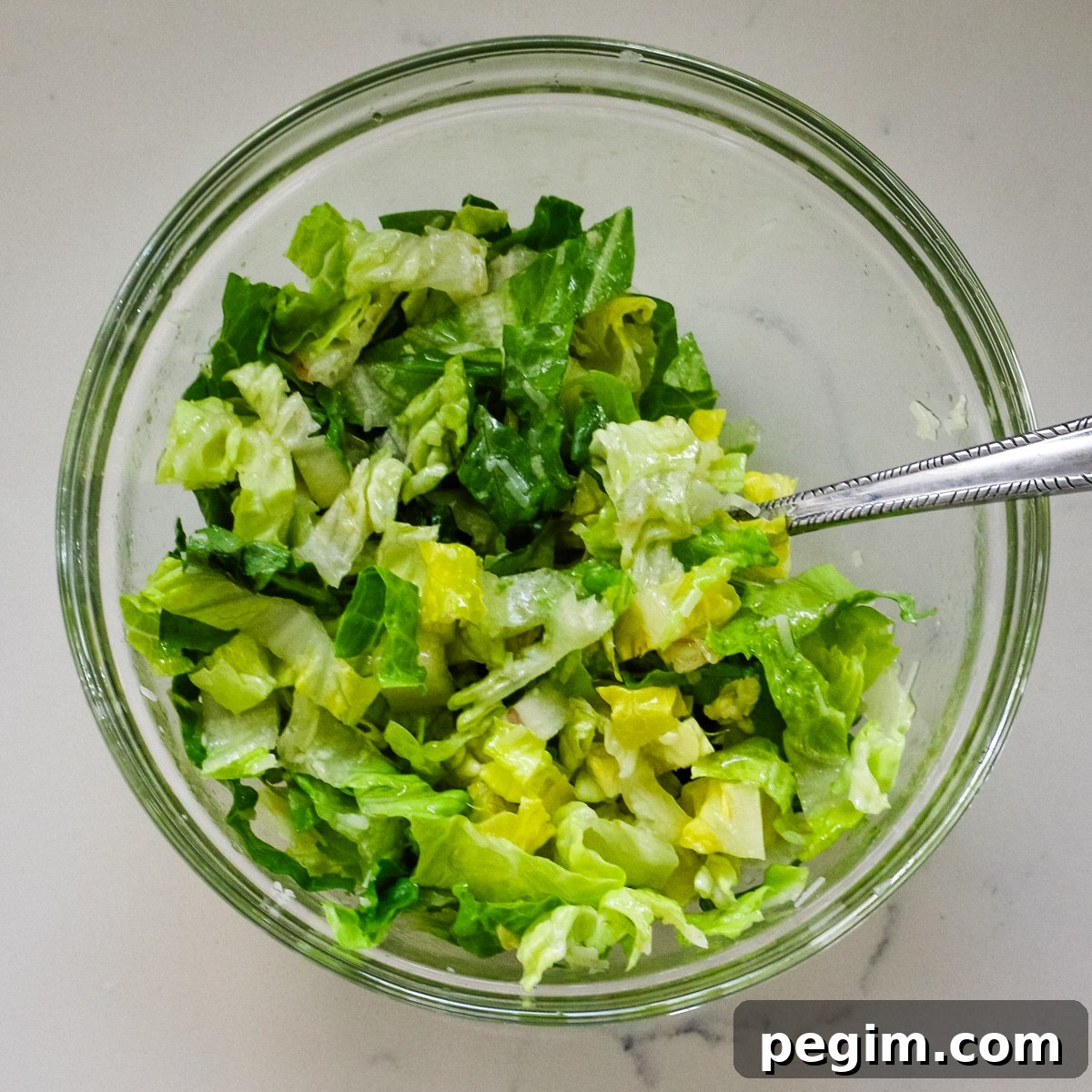 Mixing romaine lettuce in a clear bowl.