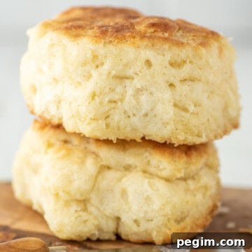 Two buttermilk biscuits on wood board with butter knife.