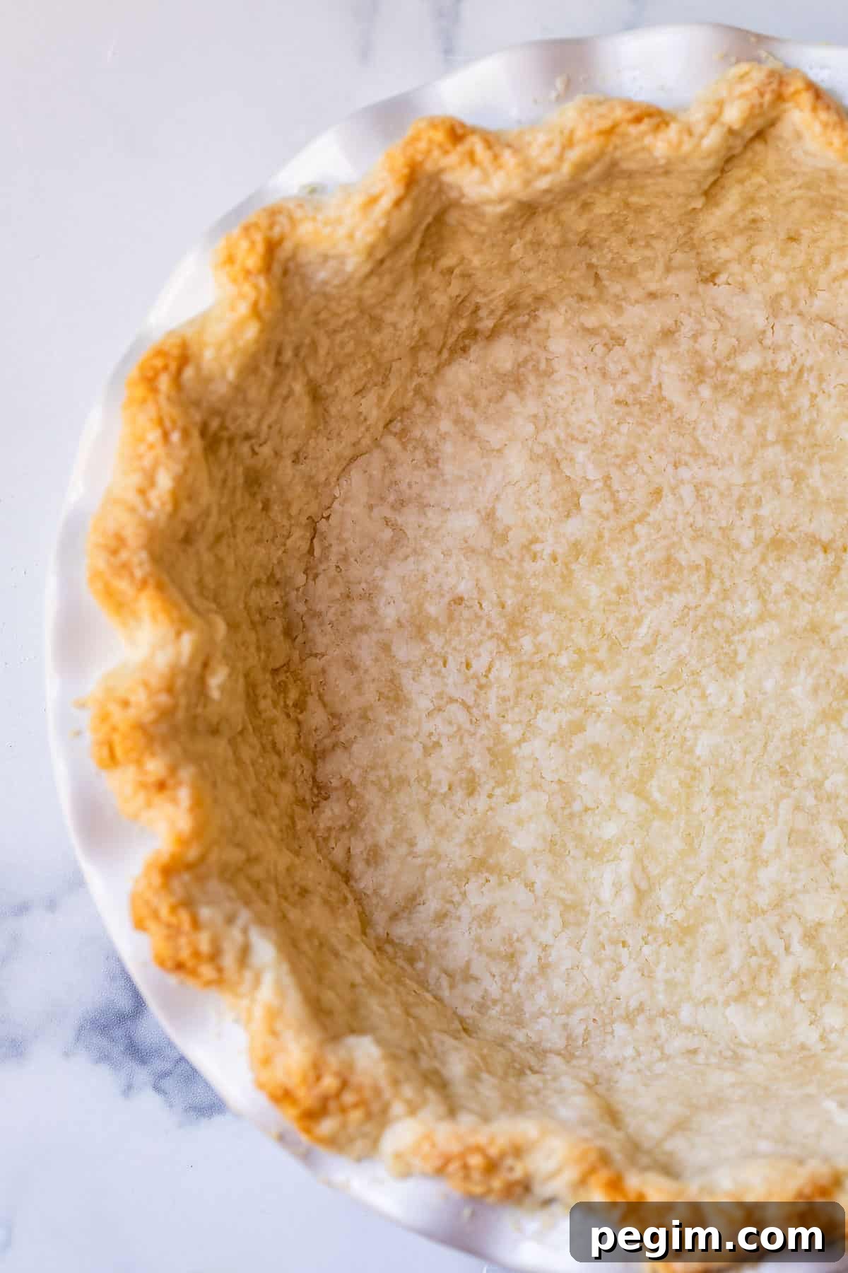 a par baked pie crust in a white pie dish on a counter, overhead.