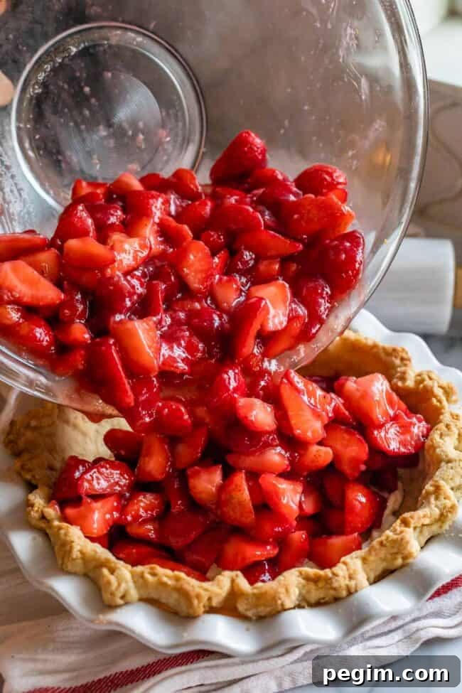 pouring strawberries into a pre baked pie shell.