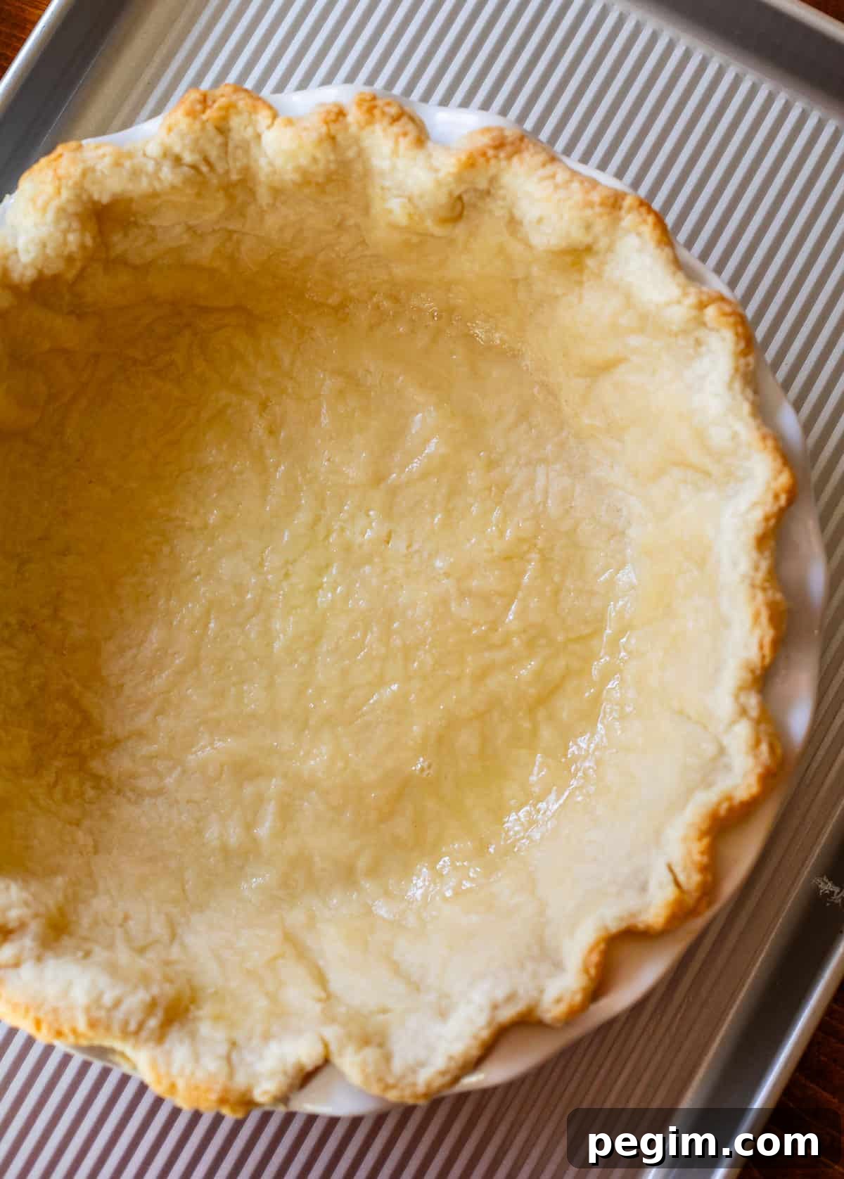 a half baked pie crust in a white pie pan on a baking sheet.