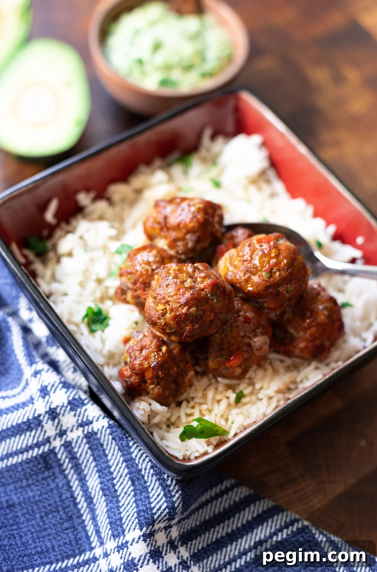 bowl containing rice topped with meatballs, avocado sauce in a dish on table. 