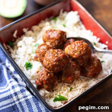 bowl containing rice topped with meatballs, avocado sauce in a dish on table.