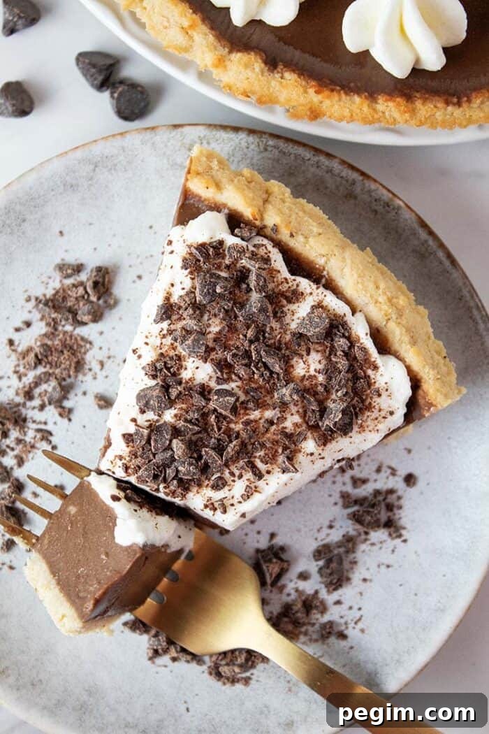 overhead view of keto chocolate pie topped with sugar free whipped cream and chocolate shavings on a swerving dish with a gold fork