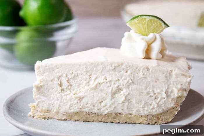 sideview of slice of keto no bake key lime cheesecake on a white serving dish topped with lime wedge and whipped cream