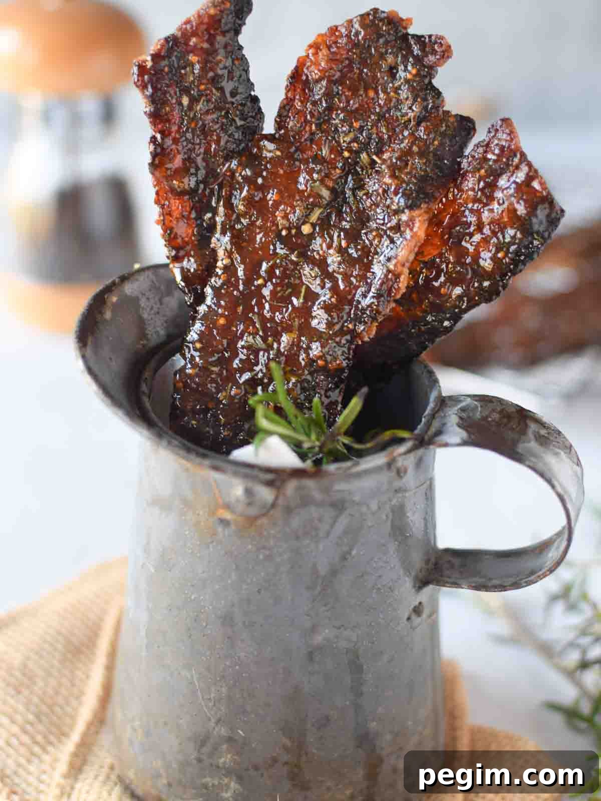 Candied bacon with rosemary and fig in a metal serving pitcher.