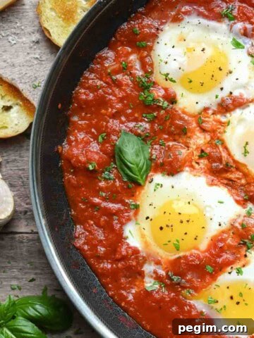 Overview of poached eggs in a skillet with tomato sauce with bread.