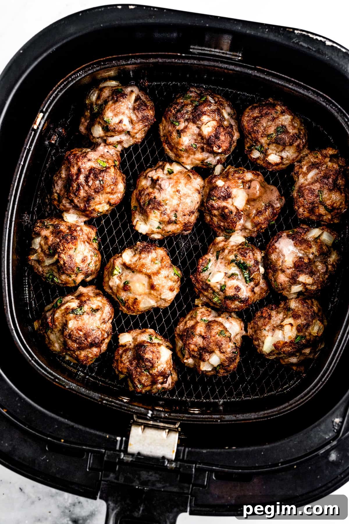 Overhead shot of meatballs cooking in an air fryer basket.