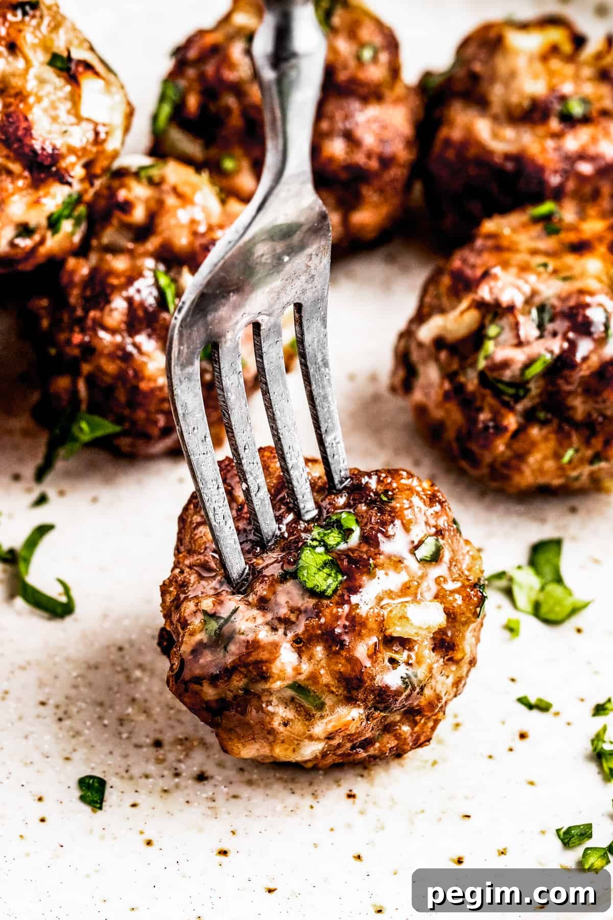 A fork piercing through an air fryer meatball served on a plate with other meatballs.