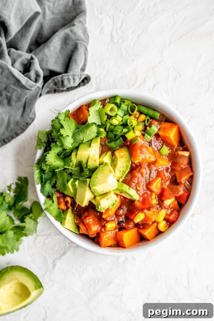 A bowl of sweet potato chili topped with avocado, cilantro and green onion.