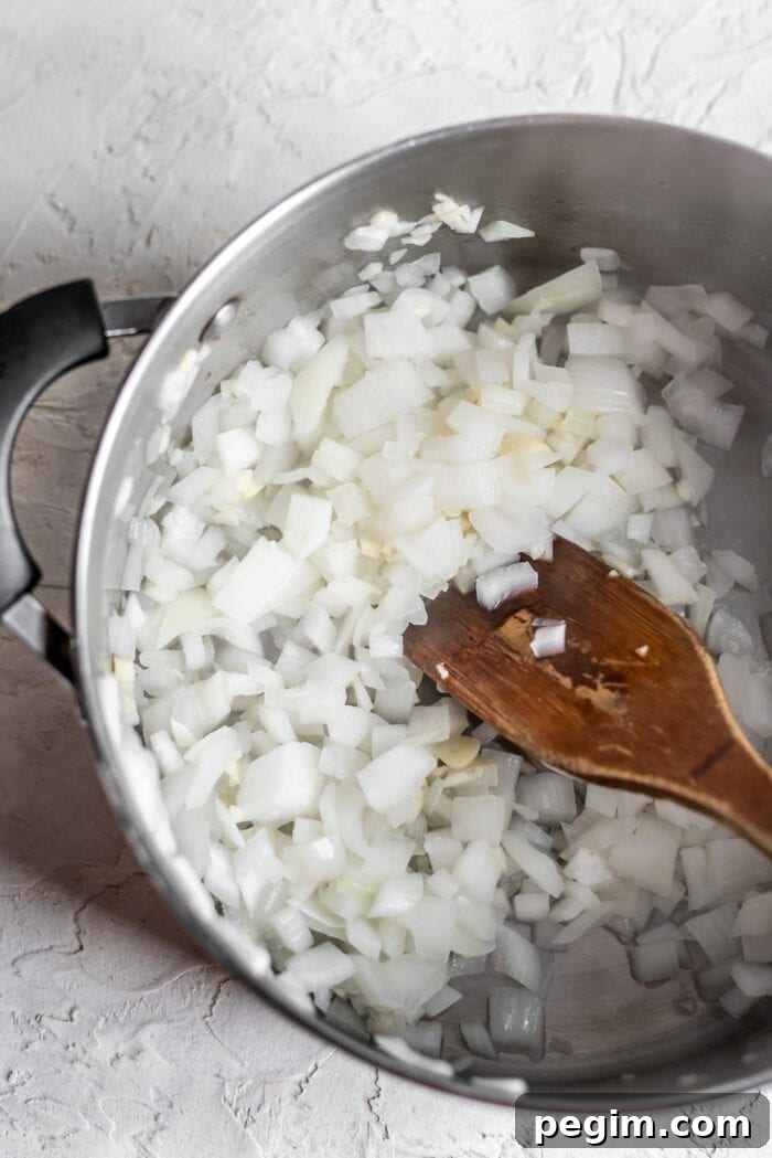 Soup pot with diced onion and garlic being mixed with a wooden spoon.