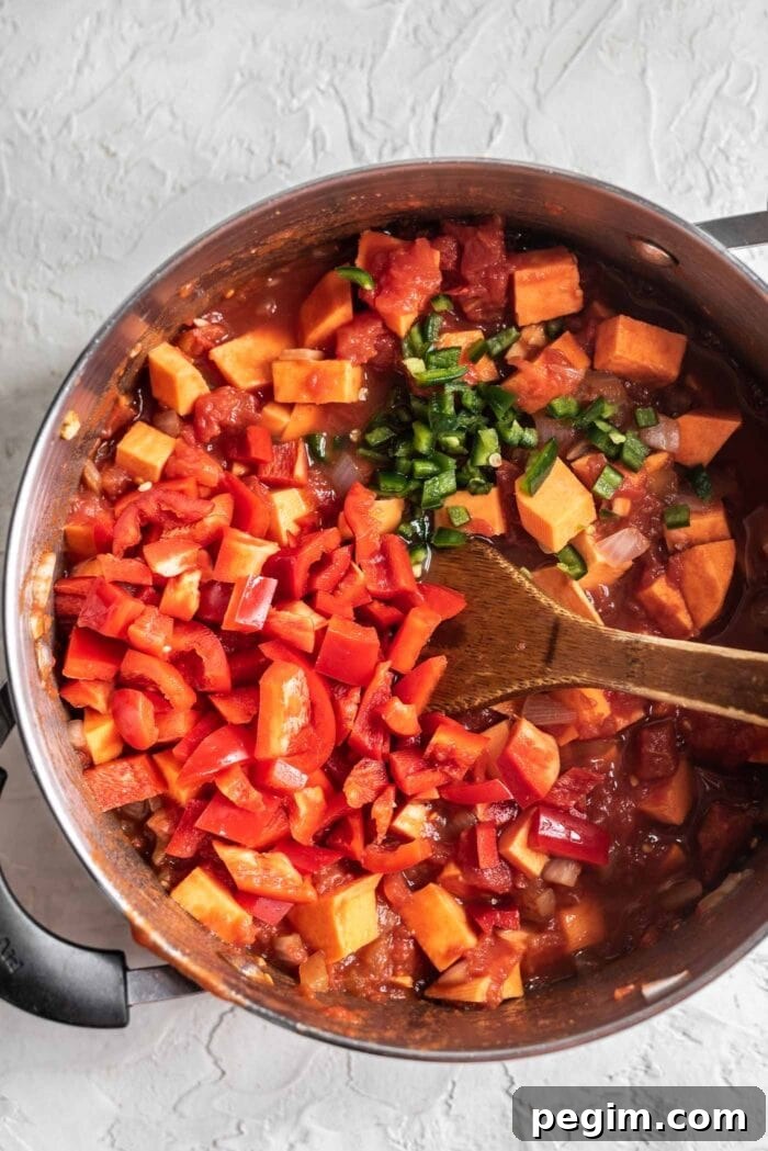 Red pepper and jalapeno being added to a large pot of chili.