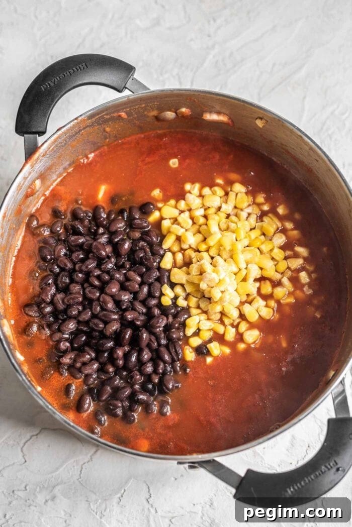 Black beans and corn being stirring into a pot of chili.