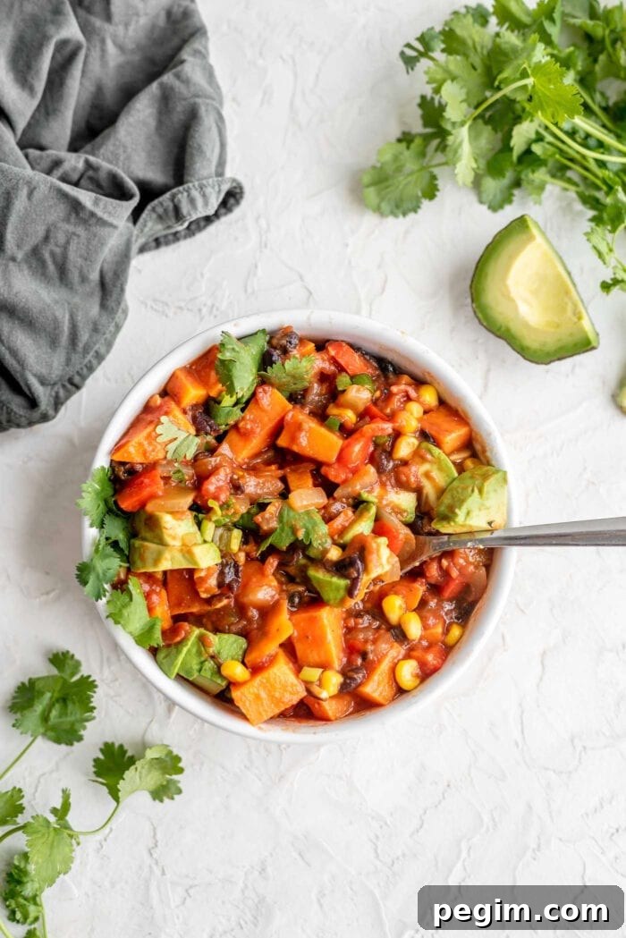 A bowl of sweet potato chili topped with avocado, cilantro and green onion.