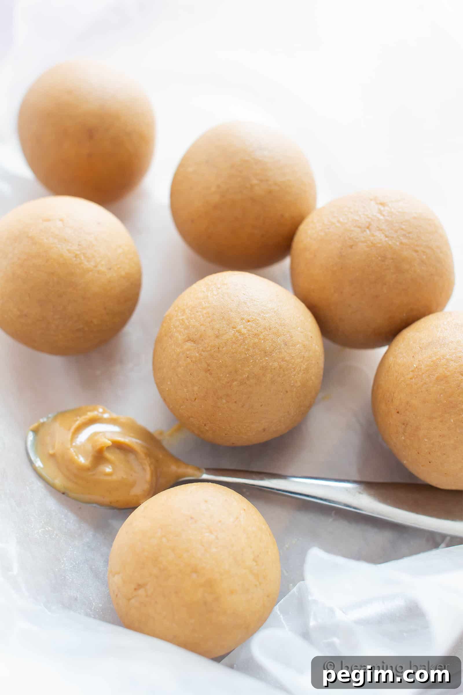 3-Ingredient Keto Peanut Butter Bites — Low-Carb Snack 4 Keto energy balls on wax paper with a silver spoon of peanut butter nearby.