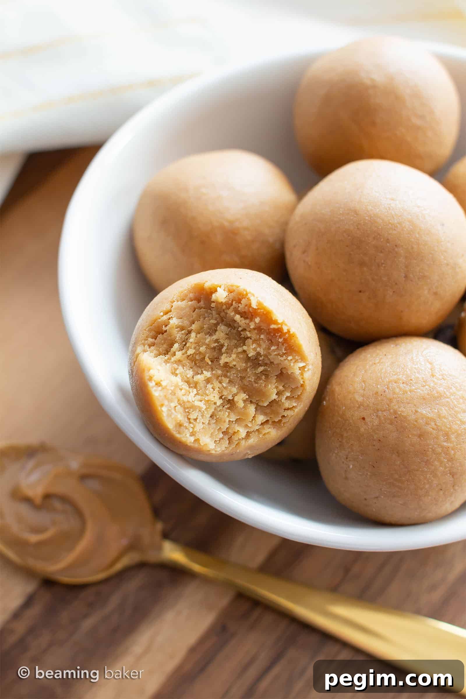 3-Ingredient Keto Peanut Butter Bites — Low-Carb Snack 5 Bowl of keto balls sitting on the kitchen counter with a gold spoon of peanut butter beneath it.