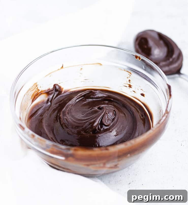 A bowl of dark chocolate ganache with a swirl on the top next to a spoon with ganache.