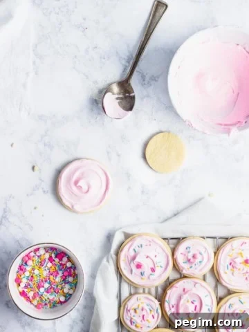 frosted cut out sugar cookies on a cooling rack with sprinkles and bowl of frosting in the background.
