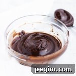 A bowl of dark chocolate ganache with a swirl on the top next to a spoon with ganache.