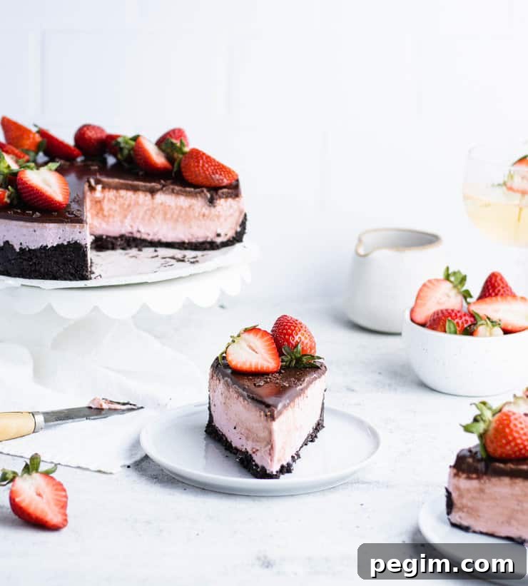Slice of chocolate strawberry cheesecake on a blue plate in front of the rest of the cake, a bowl of strawberries, a ceramic pitcher and a glass of wine.