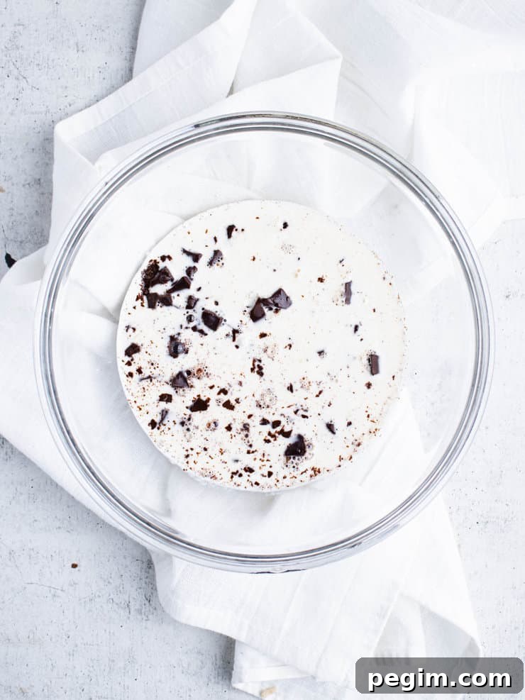 Diced chocolate covered with hot cream in a clear bowl.