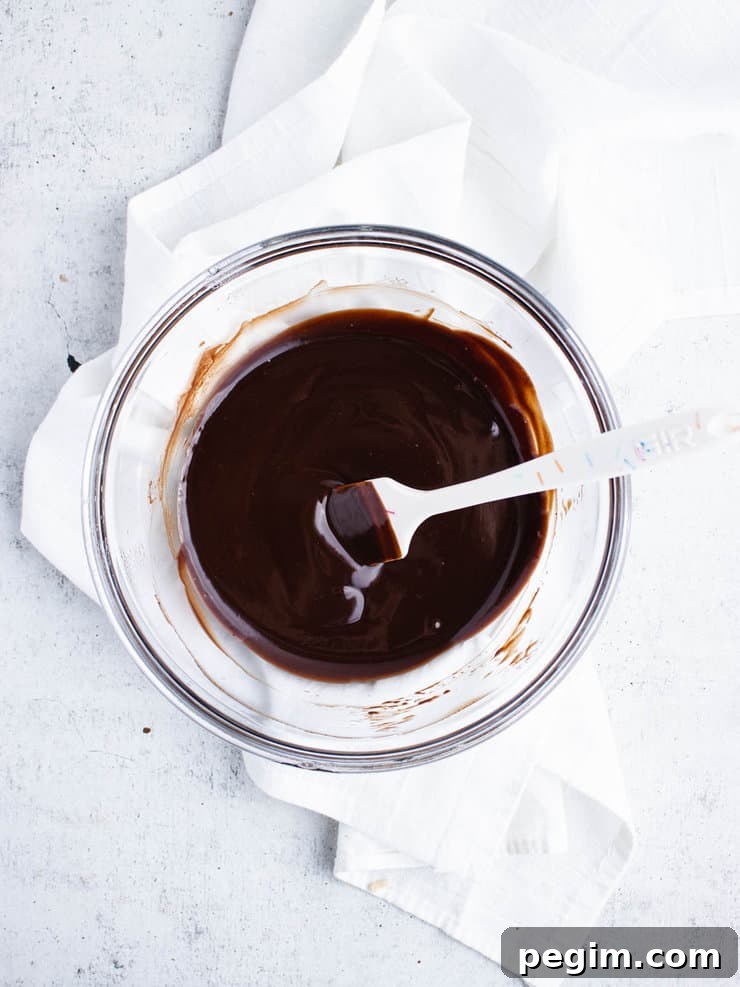 Dark chocolate ganache in a clear bowl with a white spatula sticking out to the right.