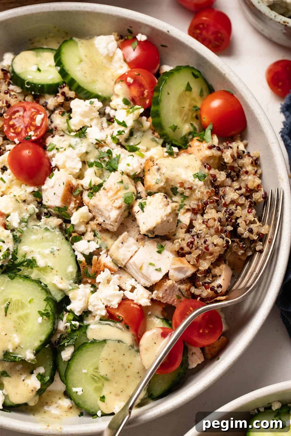 A big bowl of quinoa and chicken with Mediterranean toppings and a fork to the side. 