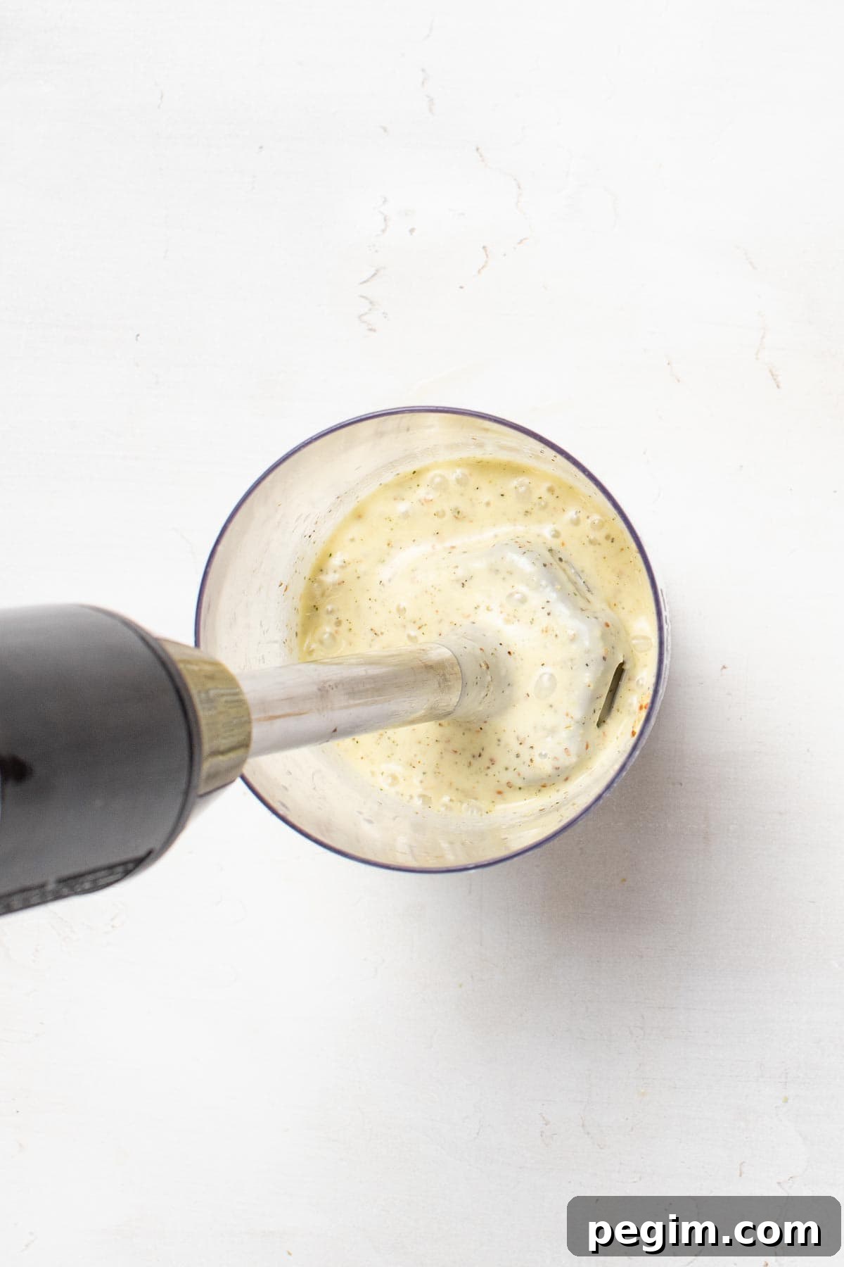 Blending olive oil and spices together with an immersion blender in a tall glass to create the vinaigrette.