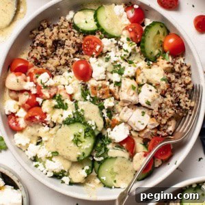 A chicken quinoa bowl with tomatoes, cucumber, and feta and a Mediterranean dressing drizzled on top.